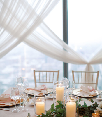 Dreamy wedding reception overlooking the downtown Indianapolis skyline. Full of floor to ceiling draping, mauve and gold accents, custom wax seal place cards, personalized place settings and a chandelier suspended above the cake table. No detail was left behind for this summer wedding at D'Amore.